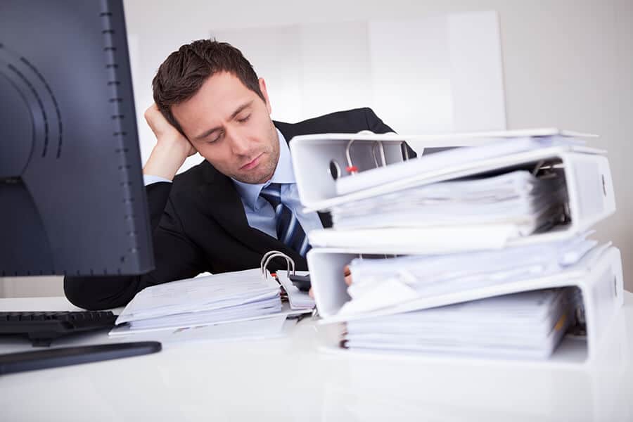 Businessman asleep at desk, in front of a stack of files