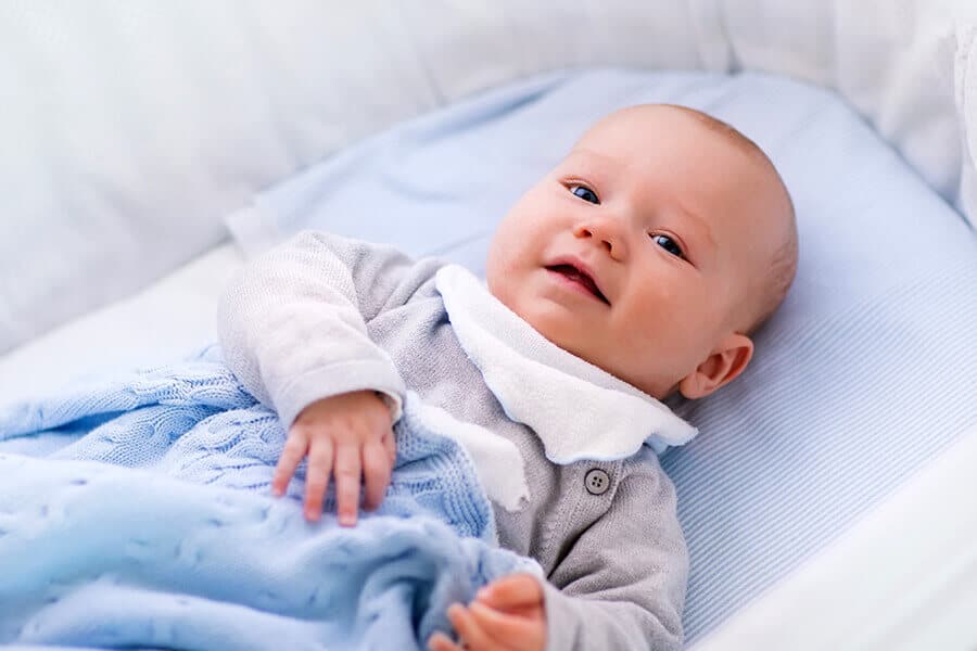 Baby in cot, covered by a blue blanket